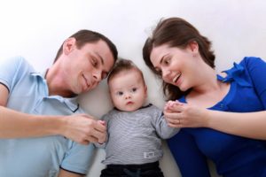 Two parents and a happy toddler laying on a bed-like surface.