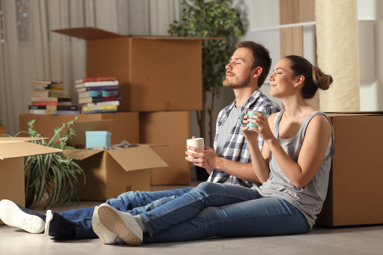 Happy couple moving home resting breathing fresh air sitting on the floor holding coffee cups